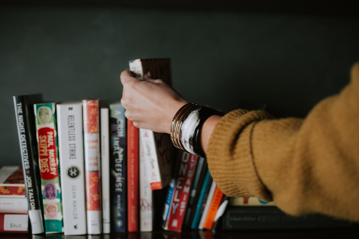 Hand selecting a book from a dark bookshelf, symbolizing careful evaluation and curation